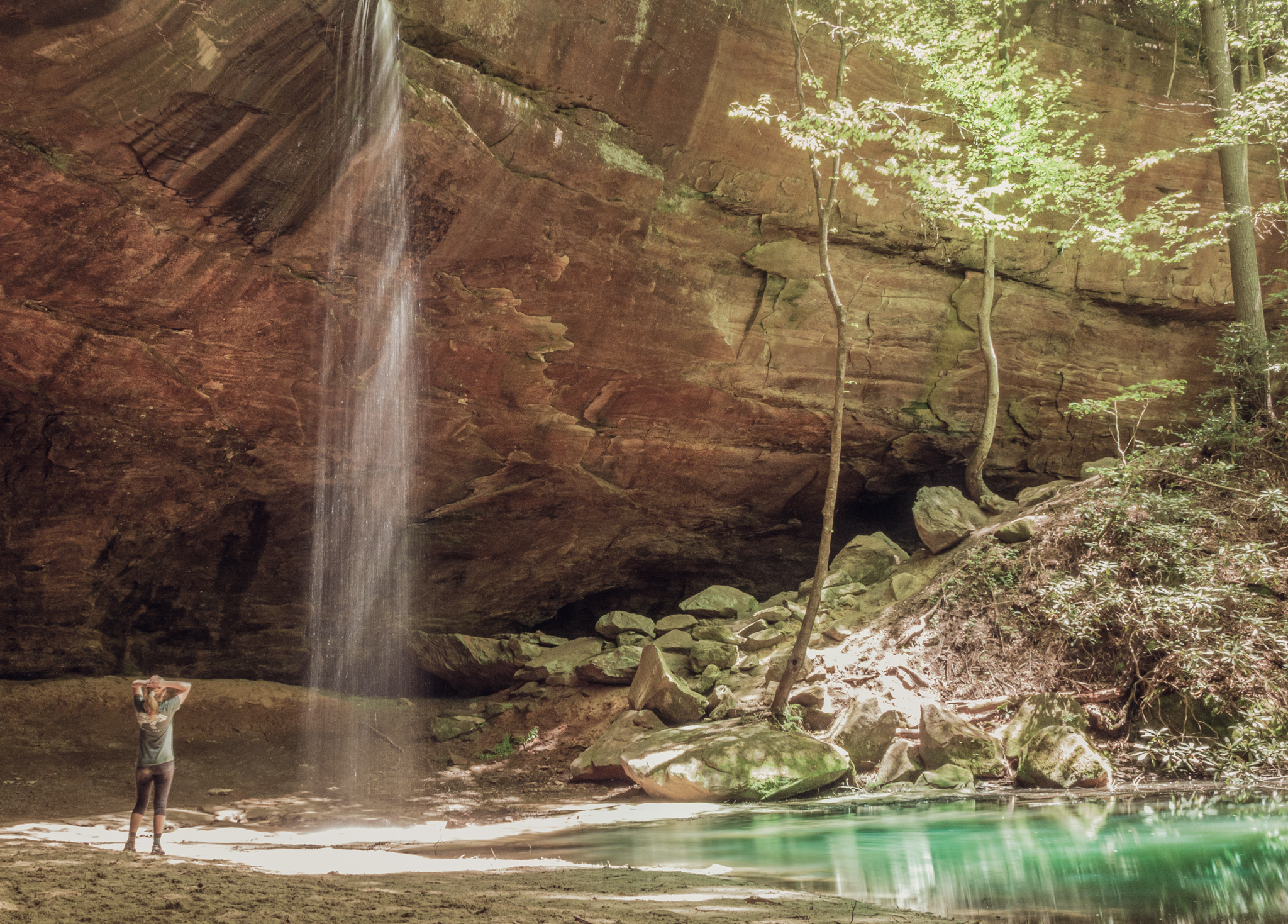 A woman stands beneath a Copperas Falls in a sandstone cave in Kentucky near the Red River Gorge