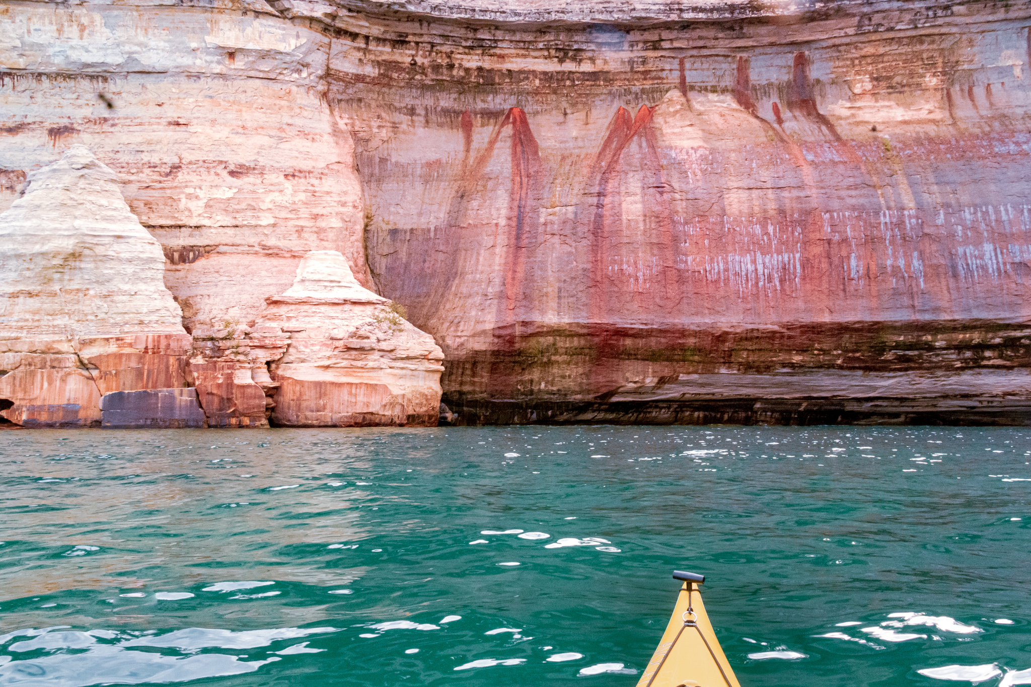 A yellow kayak on Lake Superior by the red and orange Pictured Rocks Cliffs