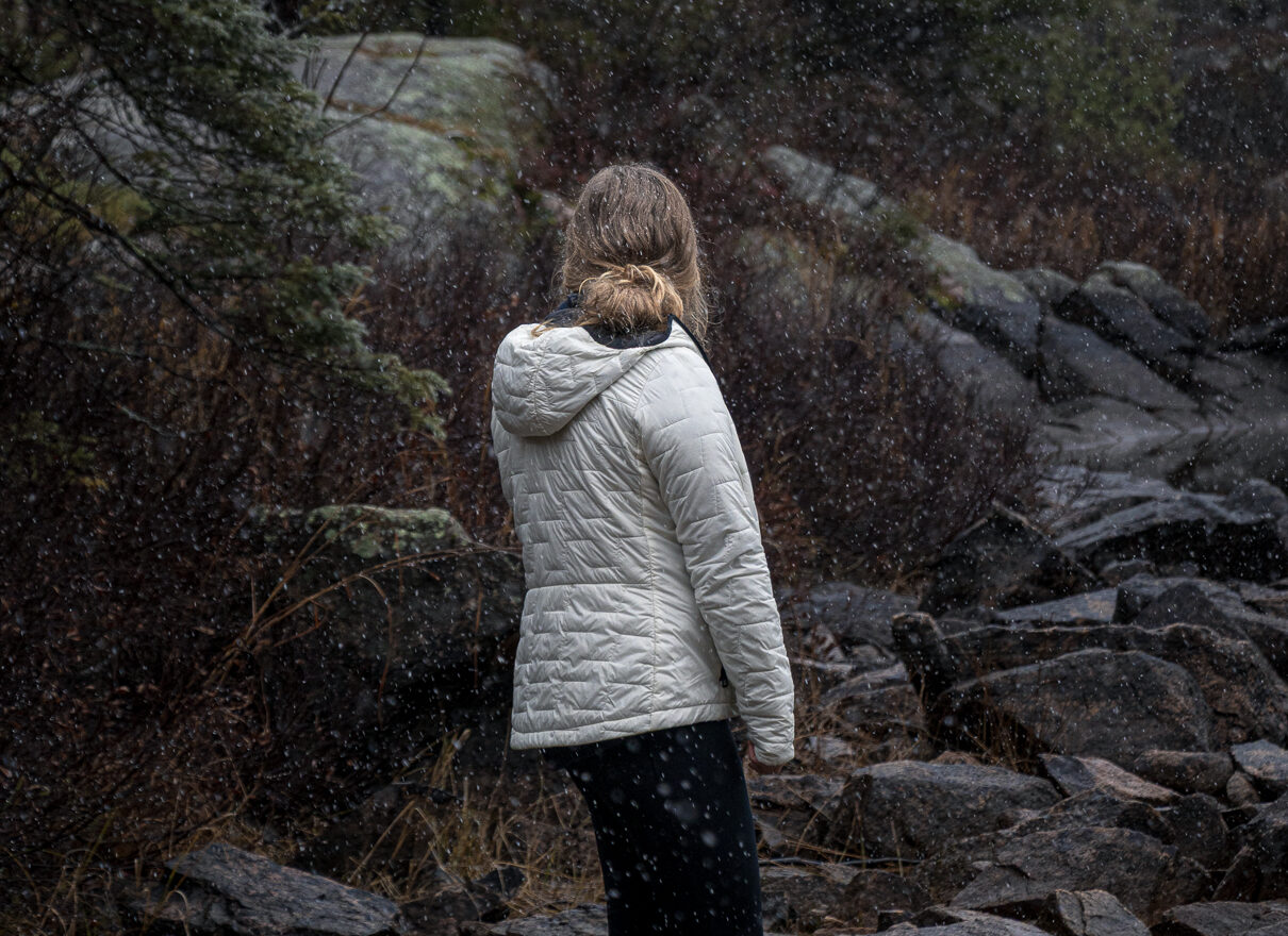 Image of a hiker in a puffer jacket standing in front of light snow in the woods